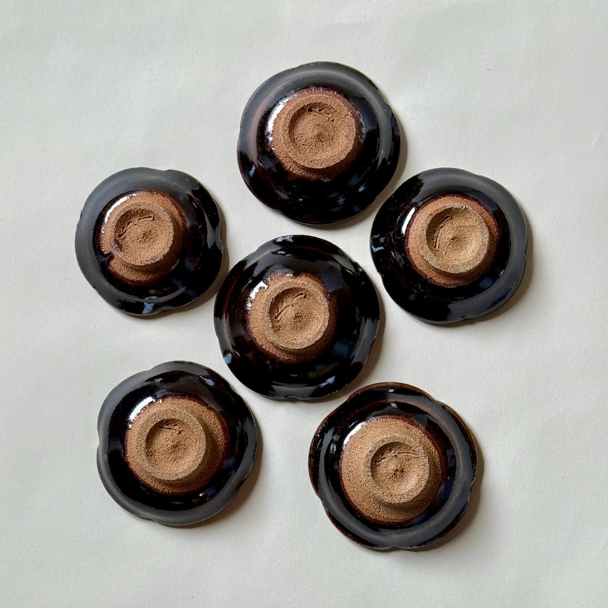 Black Karatsu flower-shaped small plates set of 6 with glossy finish and natural unglazed bases, perfect for appetizers.