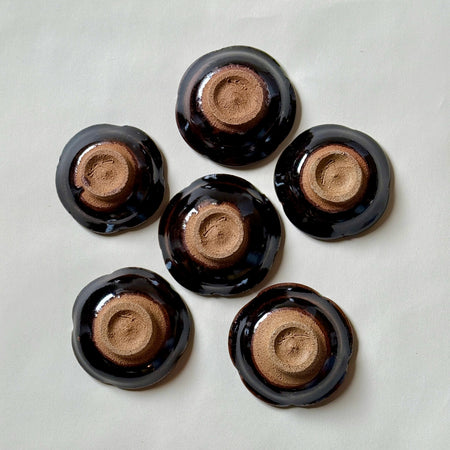 Black Karatsu flower-shaped small plates set of 6 with glossy finish and natural unglazed bases, perfect for appetizers.
