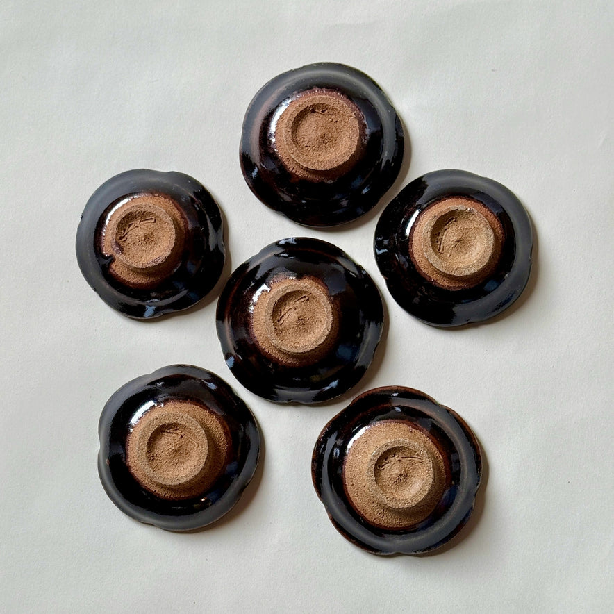 Black Karatsu flower-shaped small plates set of 6 with glossy finish and natural unglazed bases, perfect for appetizers.