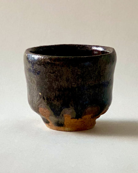 Black Karatsu sake cup with glossy dark ash glaze and rustic brown base, handcrafted by Kimiyuki with a unique texture.